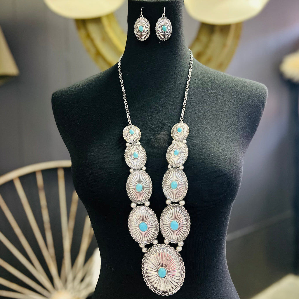   The Ranch Concho Necklace is a 32" silver necklace with stair step size conchos with  turquoise stones on each side and a 3" Concho with a turquoise stone as the Pendant.  Classy and Beautiful like you!  *matching earrings included*   