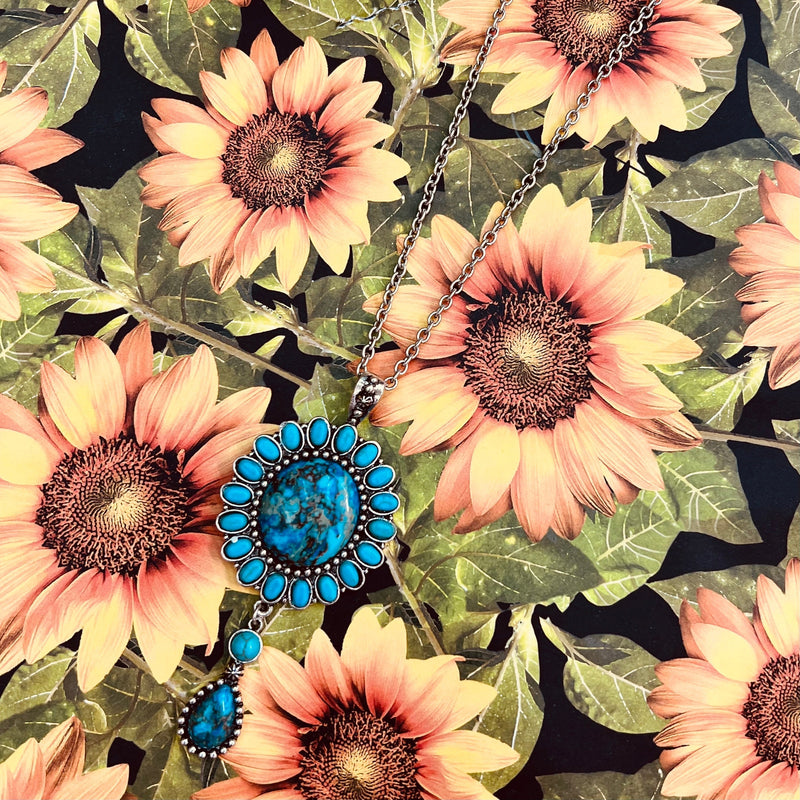 The Beautiful Blossom Necklace is a silver western necklace with a Turquoise round Pendant with a 2 stone tear drop dangle . The necklace is a 18" silver chain with a 3" adjuster clasp.  * Matching Earrings Included*