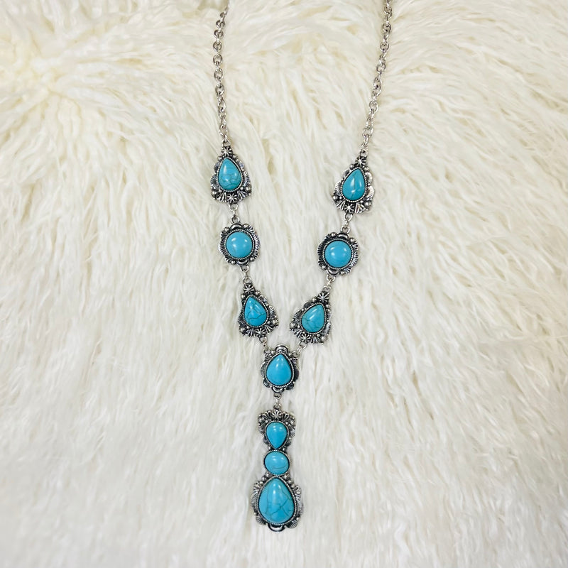 This western style turquoise stone tear drop inspired necklace is gorgeous. The tear drop shapes paired with the round stones inlayed in a silver background makes these stones stand out. The necklace is the perfect addition to any western or southwestern outfit.   20" chain with a 3" drop dangle.
