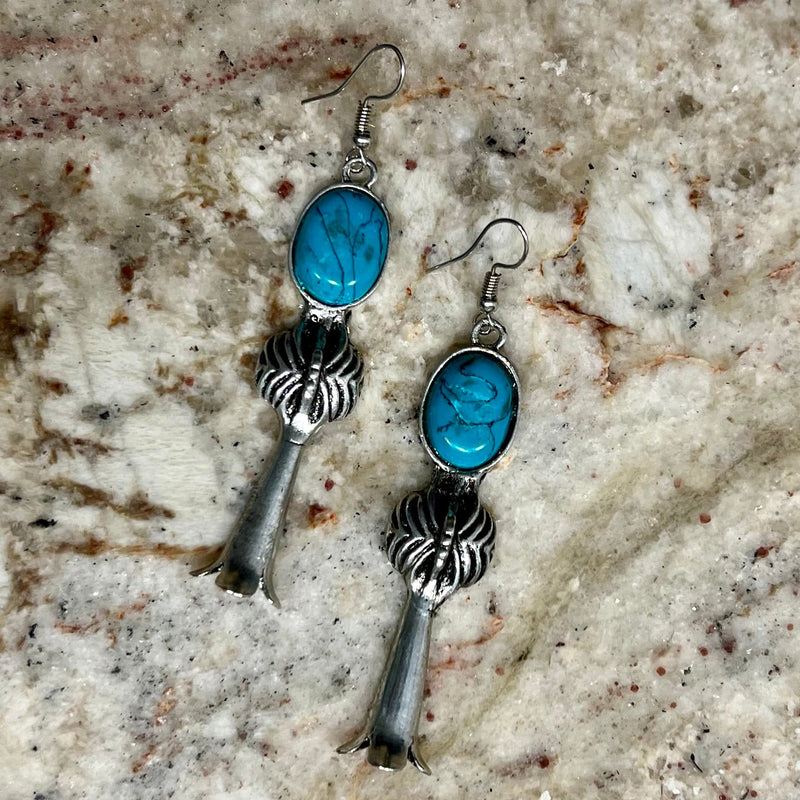 The Liberty Earrings are a 2 1/2" silver dangle earring with a flared silver bottom and a small turquoise stone set in the silver spider looking design.  They are on a fish hook back. They are 2 1/2" in total length.
