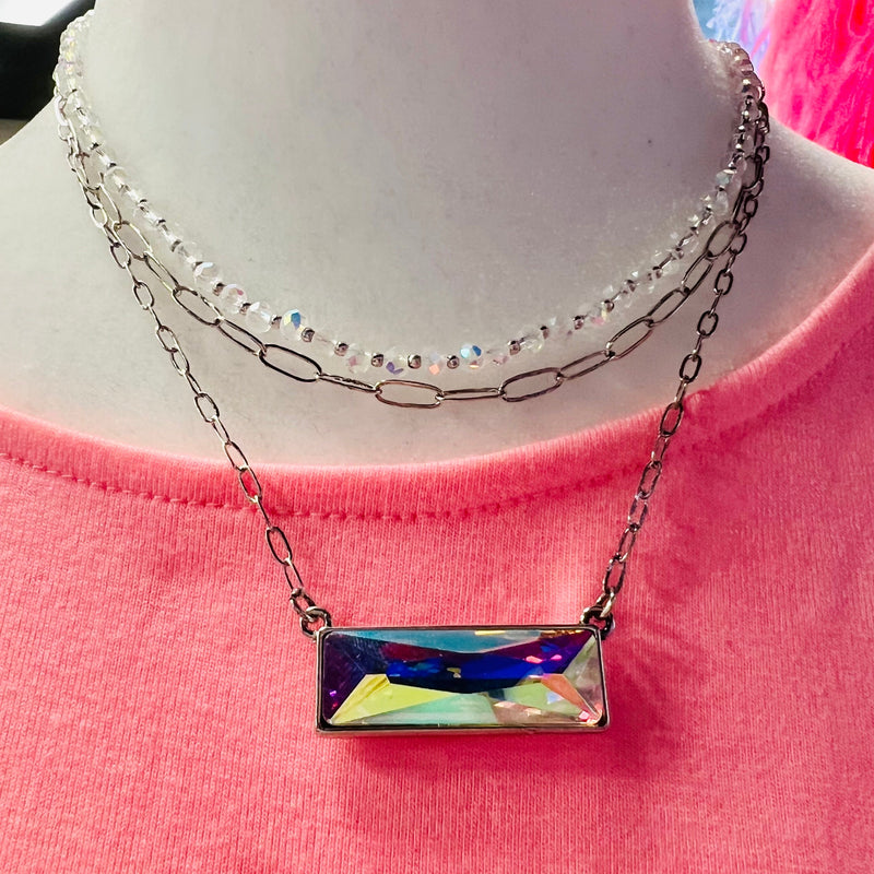 The Above The Bar Necklace is a triple strand chain link and round crystal bead necklace with a 1 1/8" iridescent bar design. The necklace is a 14" 16" and 17" chain with a 3" adjuster.