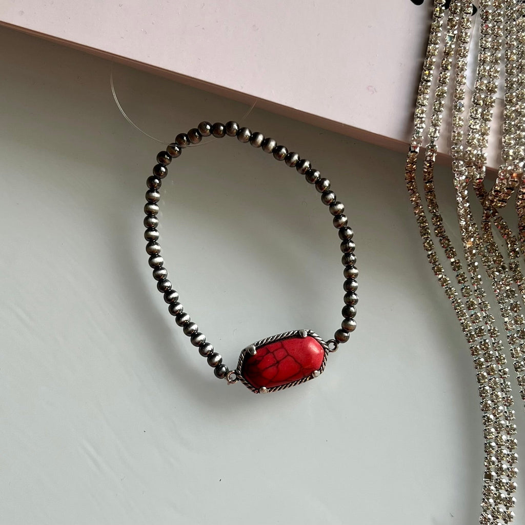In The Red Bracelet is a stunning piece of jewelry crafted with small Navajo pearls and a single 1" red stone. It is carefully handmade for a beautiful and lasting design. It is a perfect combination of fashion and tradition.