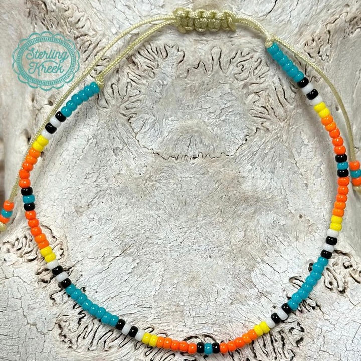 This Sahara Seed Bead Bracelet lets you adorn yourself with a stunning blend of turquoise, black, orange, yellow and white seed beads. Crafted from a single strand, it can be easily adjusted to fit any wrist size. With its classic, eye-catching design, it's a great way to add a touch of style and elegance to your look!  **Matching Sahara Seed Bead Necklace available**