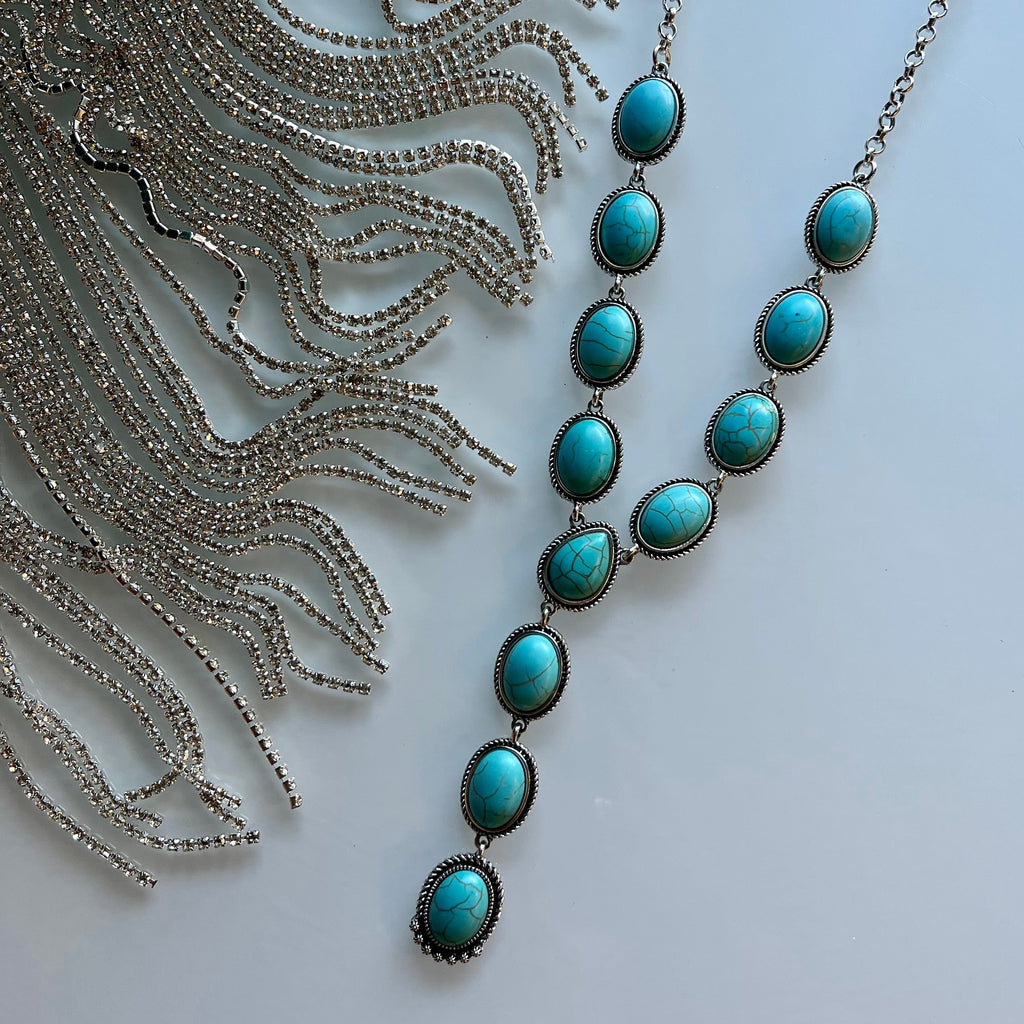This Blissfully Turquoise Necklace features 12 stones in a 4" dangle on an 18" silver-plated chain with an adjustable 3" clasp. With its unique styling, this necklace is perfect for adding a stylish and eye-catching touch to any look.