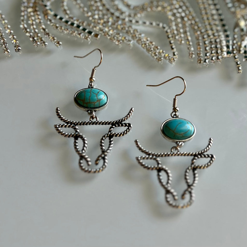 Barb Wired Bill Earrings offer a western-style twist to your everyday look. Featuring a high polish finish, twisted cable wire featuring a cow head flame set with an oval turquoise gemstone, you'll make a statement with these fish hook dangle earrings.