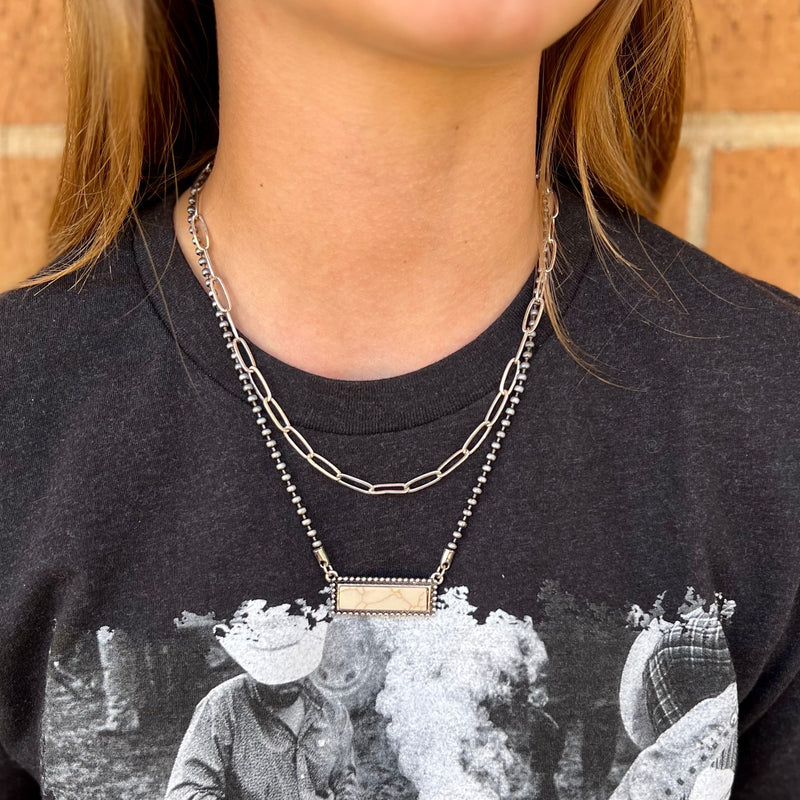 This western-style necklace features a high-polished silver rectangle bar pendant, with a double strand featuring a Navajo pearl and a chain link strand. It's a beautiful, timeless piece that effortlessly adds a fashion-forward touch to any outfit.  14" & 16" strands with 3" adjustable lobster clasp