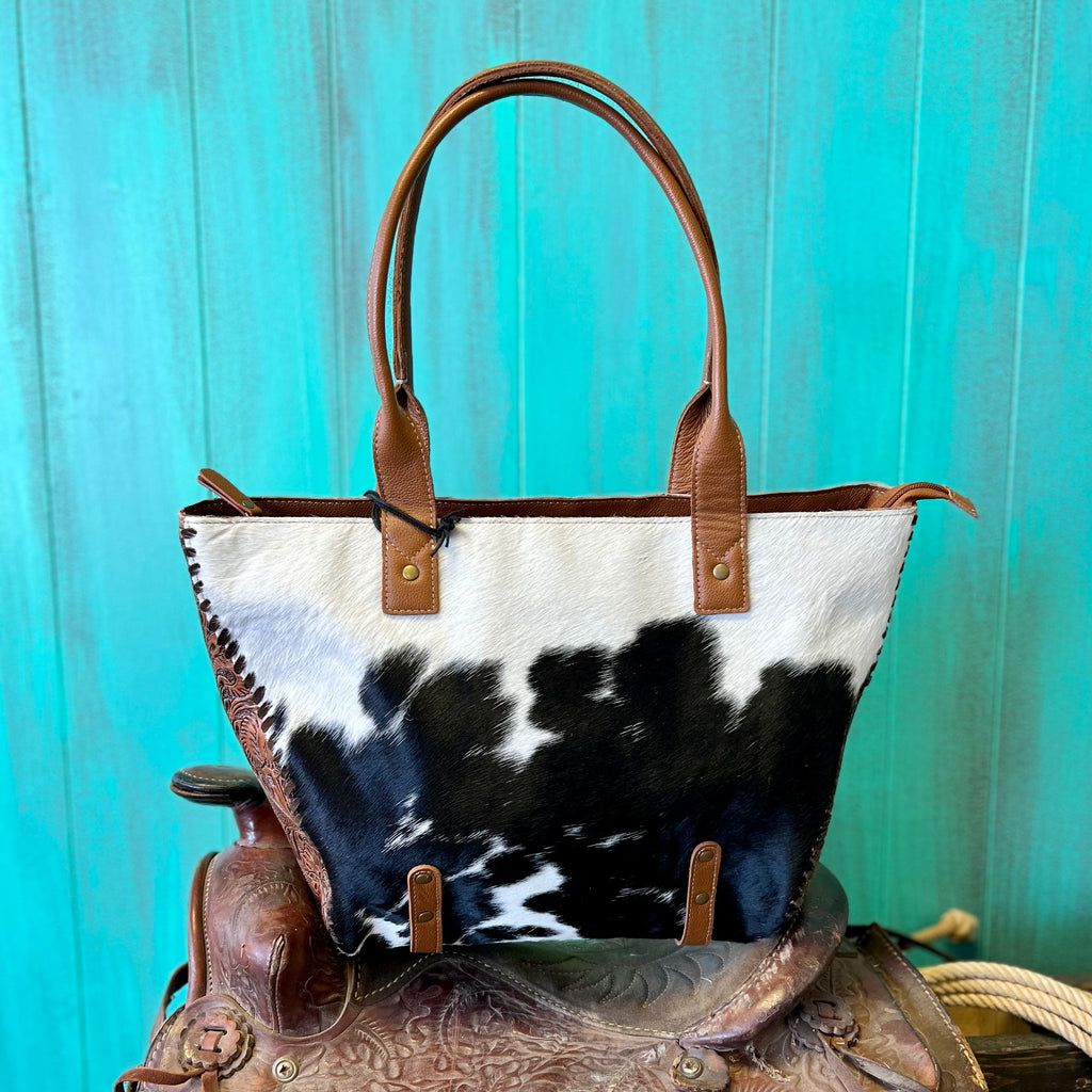 This It's All in The Stitching Handbag will stitch together your perfect look! Crafted with beautiful hair on hide, floral tooled leather detail, and 22" hand straps, it's available in three hair options for you to choose from. So go ahead, show off your unique style!  Dimensions: 17"W X 11"H