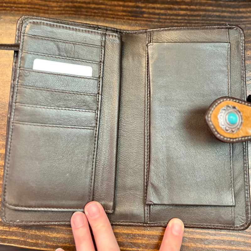 Head out in style with the Roscoe Ridge Hand Tooled Wallet! This luxurious brown leather wallet features a one-of-a-kind floral tooling, cow hide accents, and a sparkling silver flower concho with turquoise stone. You'll be looking fly with the secure fold-over flap closure to keep all your stuff safe. Now that's what I call wallet worthy!  Dimensions: 8" W X 4"H