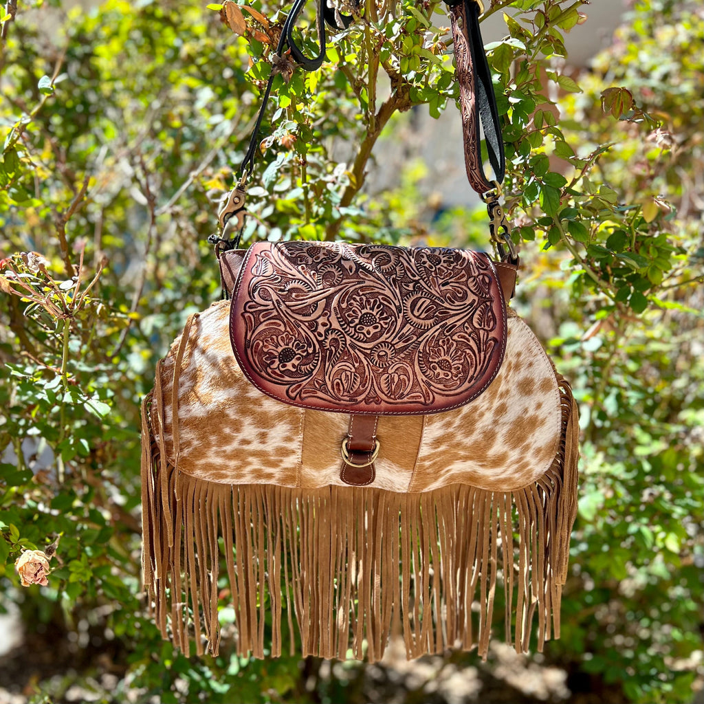 Add classic country charm to your look with this unique Leather Fringe Bag. Crafted from hair on hide and tooled leather, this bag features a timeless floral pattern and brown fringe. The adjustable 46" tooled brown leather shoulder strap lends convenience and style.  Dimensions: 15 1/2"W X 10" H