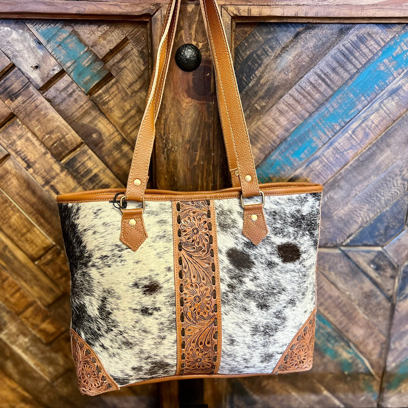 This Del Rio Hand Tooled Bag is crafted with premium grade hair on hide and detailed with floral tooled leather. Its sturdy yet supple brown leather and signature brown stitching make it a reliable everyday companion. Perfectly sized at 18W"x11H", it'll be your go-to accessory.