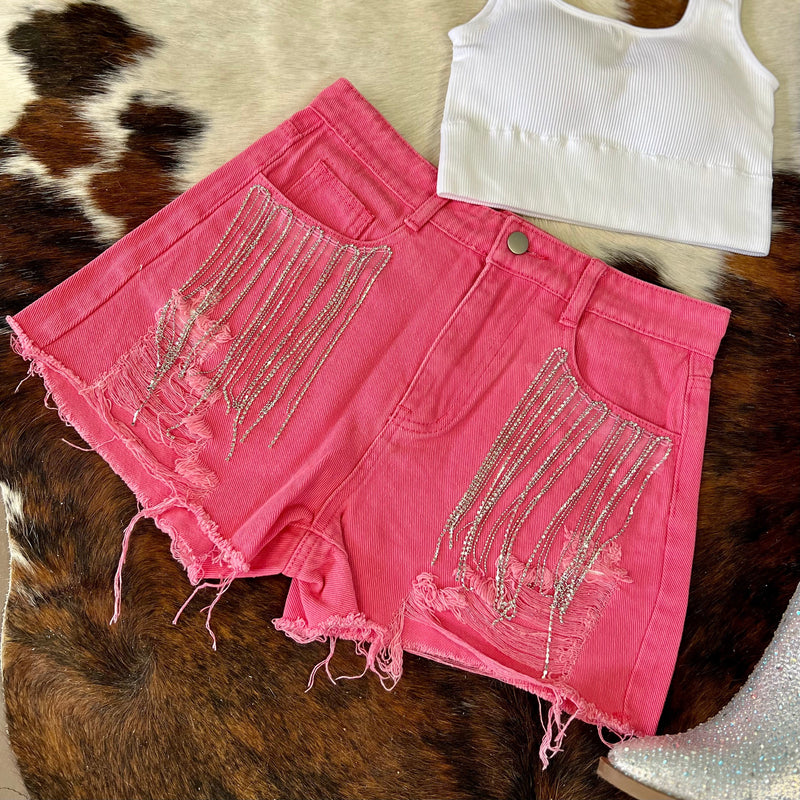 These short are made to be seen and heard! Whether you fancy Coachella or SXSW, you need these bad boys! Pink denim high waisted shorts with ripped frayed hem and rhinestone fringe detail around the front pockets.  Rise: 12"  Inseam: 4"  90% Cotton, 10% Polyester