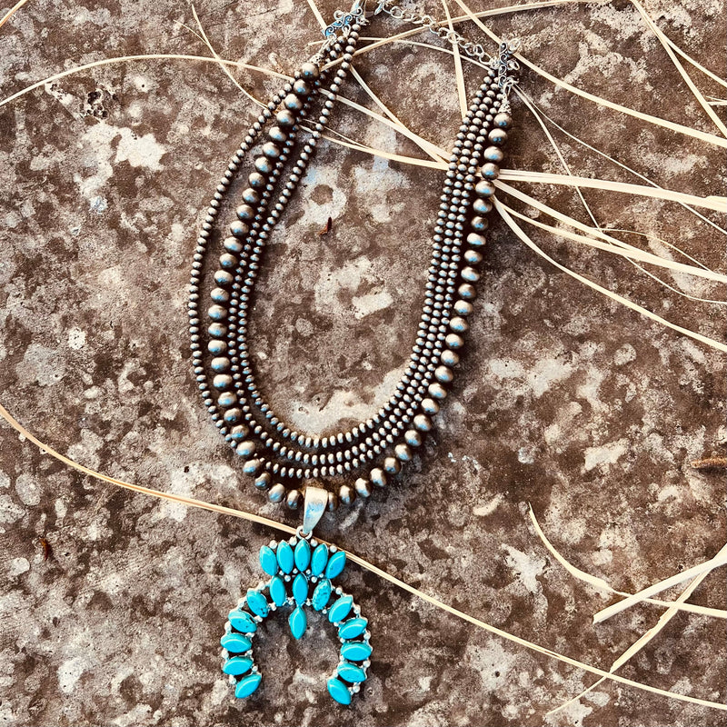 The Turquoise In The Wild Necklace is a 18" long, tiny navajo pearl & squash blossom natural turquoise pendant necklace. The stones very in size, color, and shape. The 4 strand necklace is a 18" necklace with a 5" extender. The Pendant is 2 1/2" long.