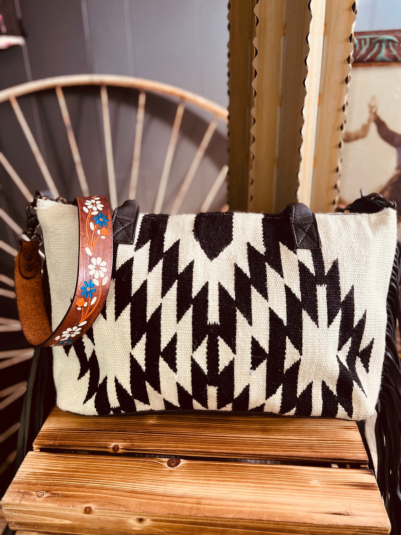 No Grey Area Fringe Bag is a Black and White Diamond Aztec Saddle Blanket Bag. It has a gorgeous 42" floral painted tooled detachable leather strap and black fringe down both sides. It is 19" L X 11" H. 