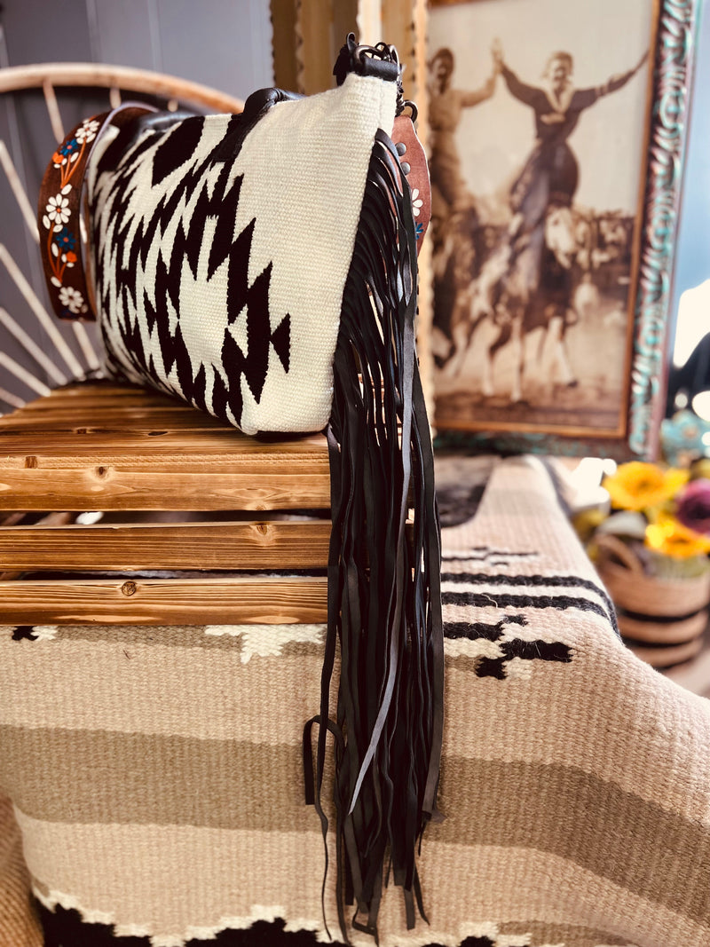 No Grey Area Fringe Bag is a Black and White Diamond Aztec Saddle Blanket Bag. It has a gorgeous 42" floral painted tooled detachable leather strap and black fringe down both sides. It is 19" L X 11" H. 