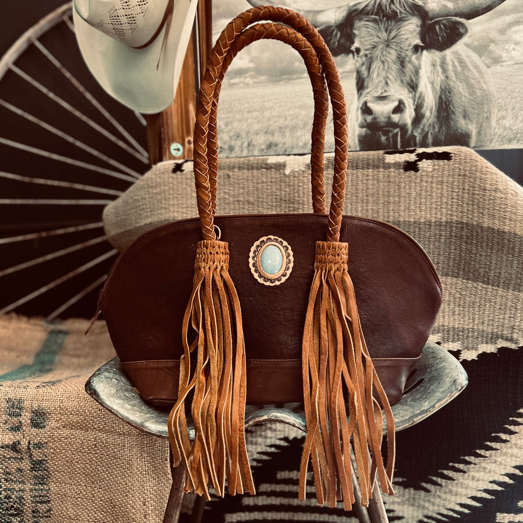 The Darling Wide Mouth Handbag is a genuine soft brown leather bag. The bag has braided 24" handles and a 54" removeable shoulder strap.  There is also braided detail attached to the fringe. The purse measures approx. 20" L X 10" and the zipper closure opens up very wide for easy storage. They are several inside compartments to keep your items secure.