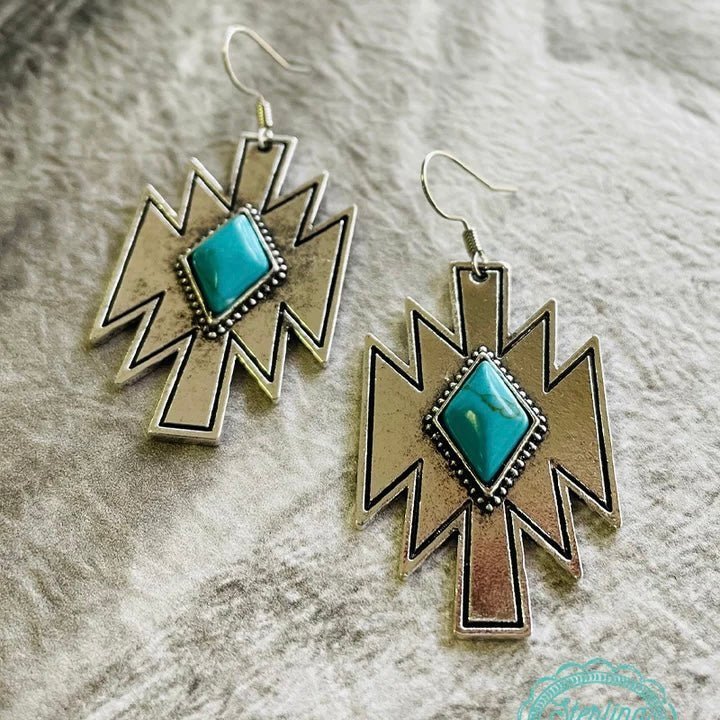 The Choctaw Nation Earrings are a Beautiful Silver Aztec Cutout with a Turquoise Stone in the center. The total length of the dangle is 2" from fish hook.