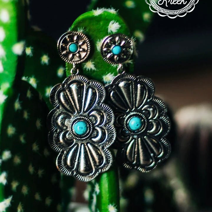 The Western Darling Earrings are a Beautiful New Silver Stamped Dangle with 2 turquoise stones. The small post back with a circle silver design with a small turquoise stone connected to a 2" silver dangle stamped designed piece with a turquoise stone in the center. Total length of the earrings is 3". 