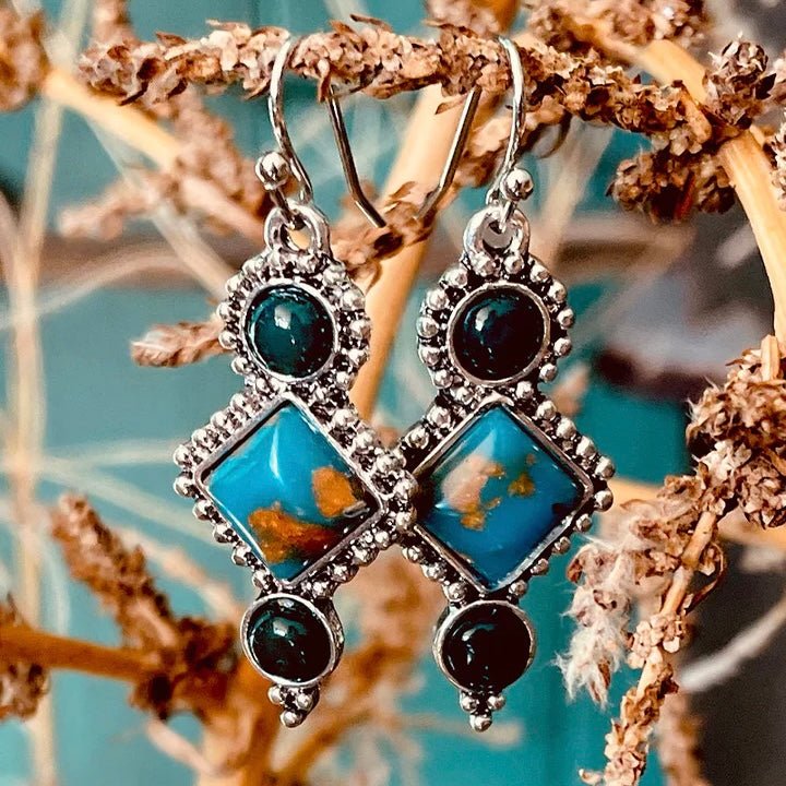 The Gypsy Gem Earrings are a 3 stone dangle earring on a fish hook back. The center stone is a turquoise and brown authentic stone with 2 small green stones on top and bottom. The total length is 1 1/2" long. 