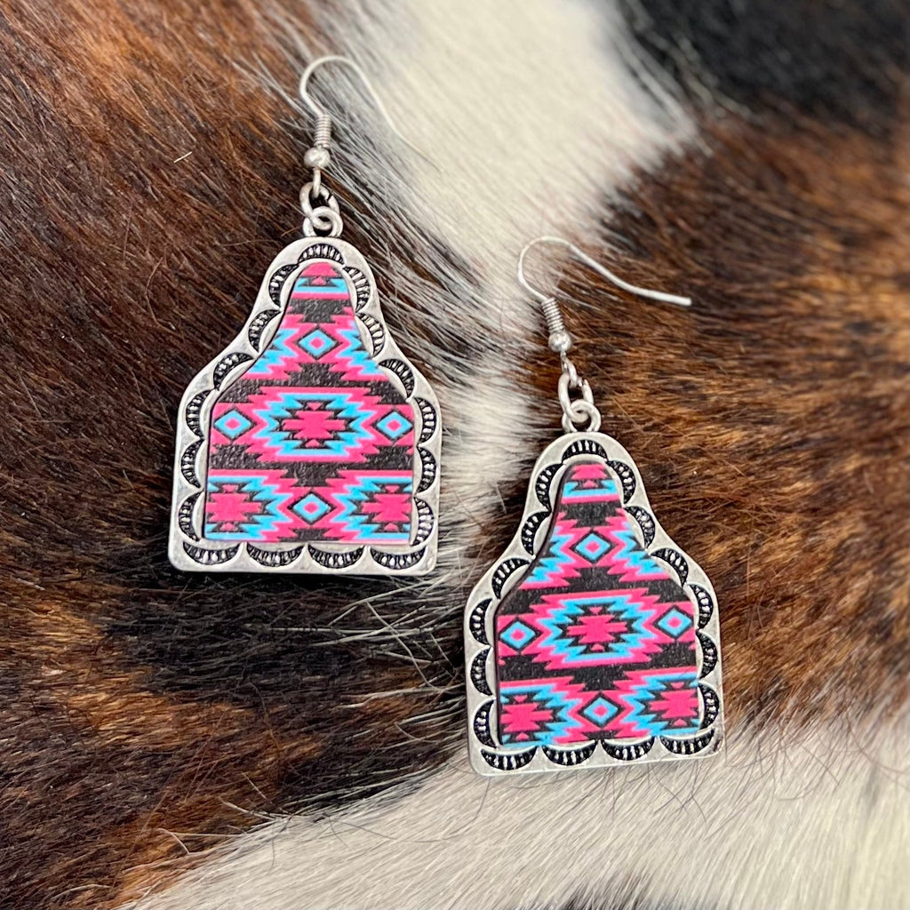 The Glenwood Earrings are a cow tag silver cutout stamped on the edges. These earrings have 2 variants; one set with bright multi colored Aztec design in the center, and another with turquoise, brown, and red Aztec design in the center. Super cute light weight earrings. 1 3/4" in total length.