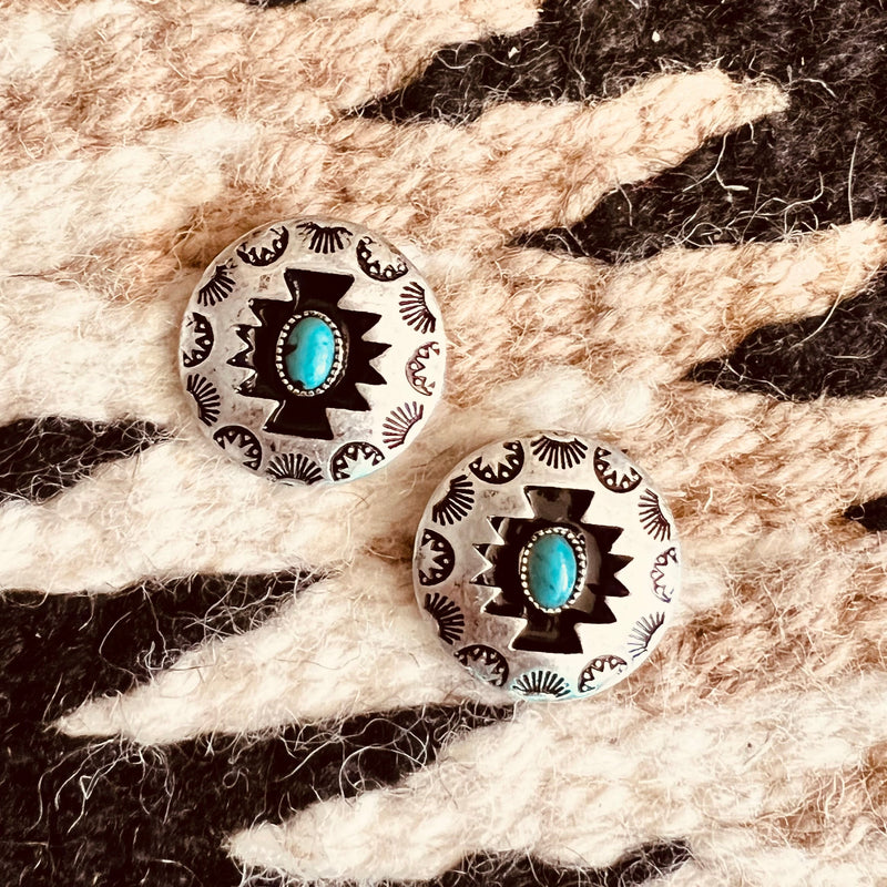 The Concho Style Aztec Silver stamped post back earrings feature a small turquoise stone inlayed in the center. The tribal Aztec stamp design around the edge makes these earrings pop. The Aztec design is black and makes the small turquoise stone stand out.  These earrings are 1" in diameter. 