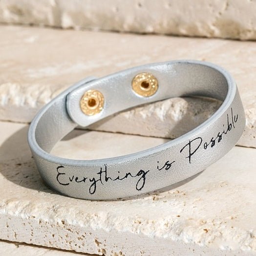 Silver faux leather thin strap bracelet with black script saying " Everything is possible". Snap button closure.