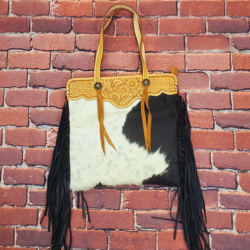 Hair on hide leather shoulder bag with hand tooled straps and top trim. Features decorative concho with tassel and black suede fringe down sides. One large outside zipper pocket, one large inside zipper pocket, and two inner open pockets. Back is black leather. Includes removable cross body strap. H17"xW17" 10" handles