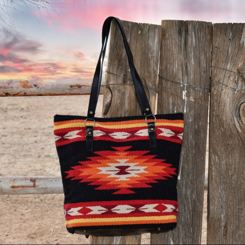 Handwoven of imported 100% wool saddle blankets in classic Zapotec style. This handcrafted handbag is a Southwest style favorite.  Zipper closure, fully lined inside, interior pocket and racoon tail embellishment. Bottom and handles are black vegan leather. Bottom has metal feet. All black back in wool saddle blanket.