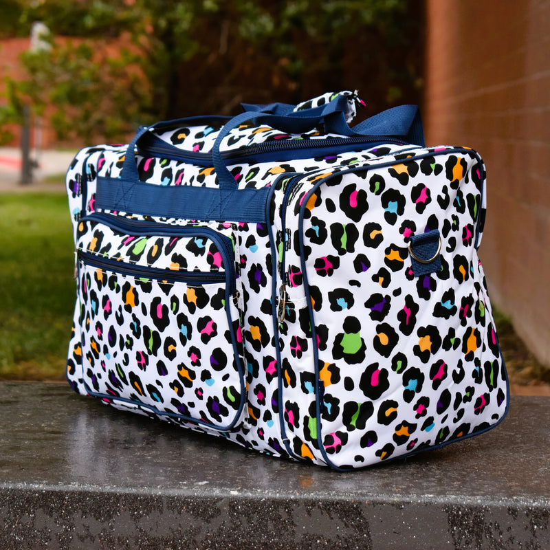 White nylon duffel in bright colored leopard spots. This travel or gym bag has zipper top closure, zipper pockets on each side, two front pockets with zippers, two navy carrying handles, and a navy shoulder strap that can be removed. Plastic feet for cleanliness. 