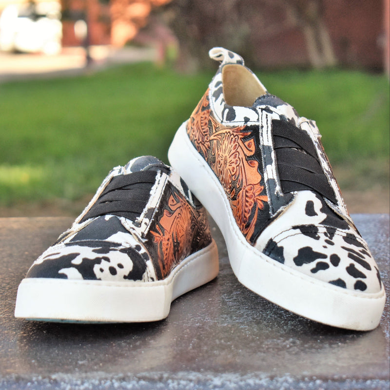 Give your feet some style with these classic black and white cow print & tooled leather flat sneakers. They'll be your go-to pick for casual office days, shopping, or dress them up for a night on the town. 