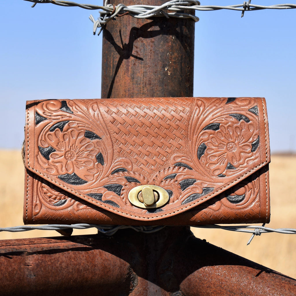 Large tan embossed leather wallet in floral and basket weave prints and painted black detailing. Brass toggle clasp closure on the envelope front flap.