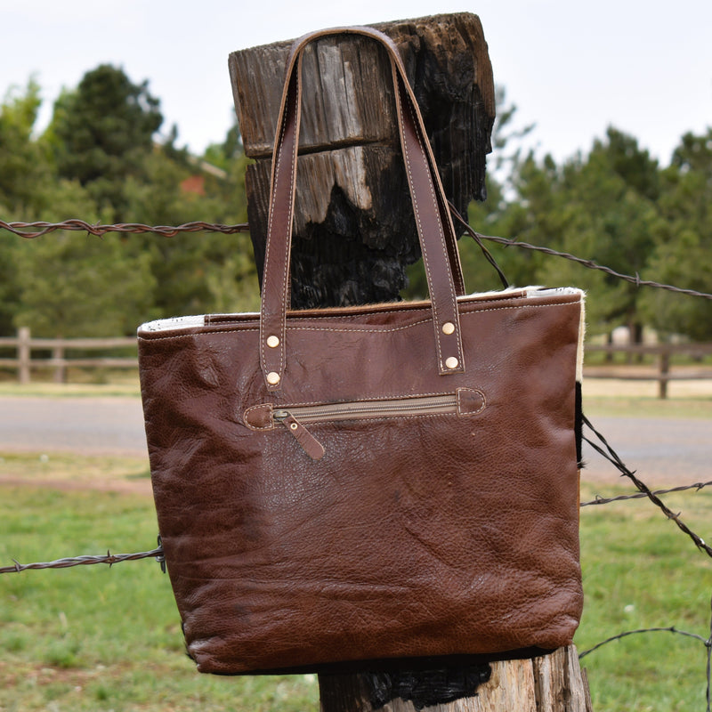 100% genuine leather and hair on hide handbag with six patchwork hair on hide sections in the front, and brown pebbled leather for the back and handles. Back zipper pocket. Front has decorative brass grommet snap details.