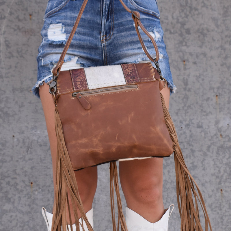Calling all cowgirls! This long strap cross body bad has a hair on hide front, with brown leather back and strap. Strap is adjustable and removable, and back features a zipper pocket. Over the zipper top is a leather flap closed with a center magnetic button, with a suede buckstitch lacing edged flap with a center of hair on hide flanked in tooled strips of leather that feature a sunflower design. Suede side fringe and brass ring with a long suede tassel adds that extra dash of frontier spirit!