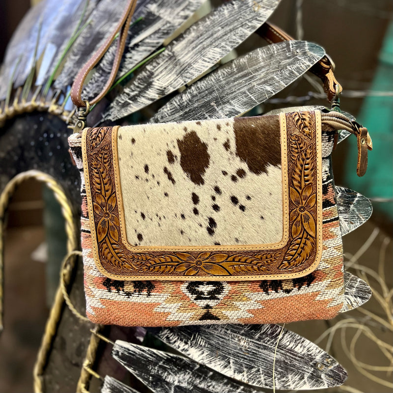 Made By Myra Handbags  The White Sands Bag is Southwestern Aztec Western Saddle Blanket Pattern with a Hand Tooled Leather Detail. This bag has a top zipper closure and a small zipper compartment of the back side.  The back side of the bag is a fawn colored cotton material that is soft and durable. The strap is a " and is adjustable/removable.  Dimensions: 12"W X 10"H  Strap: 22" Adjustable/Removeable Strap
