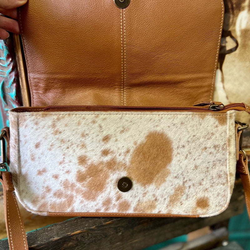 Made by Myra Handbags  The Los Lunas Cross Body Bag is a Beautiful Cowhide Purse with a Hand Tooled fold over flap. The Bag offers 3 different cowhide variants. This bag has a top zipper closure with a fold over flap.  The strap is a 44" and is adjustable/removable.  Dimensions: L 11" X H 6"   Adjustable up to 44"