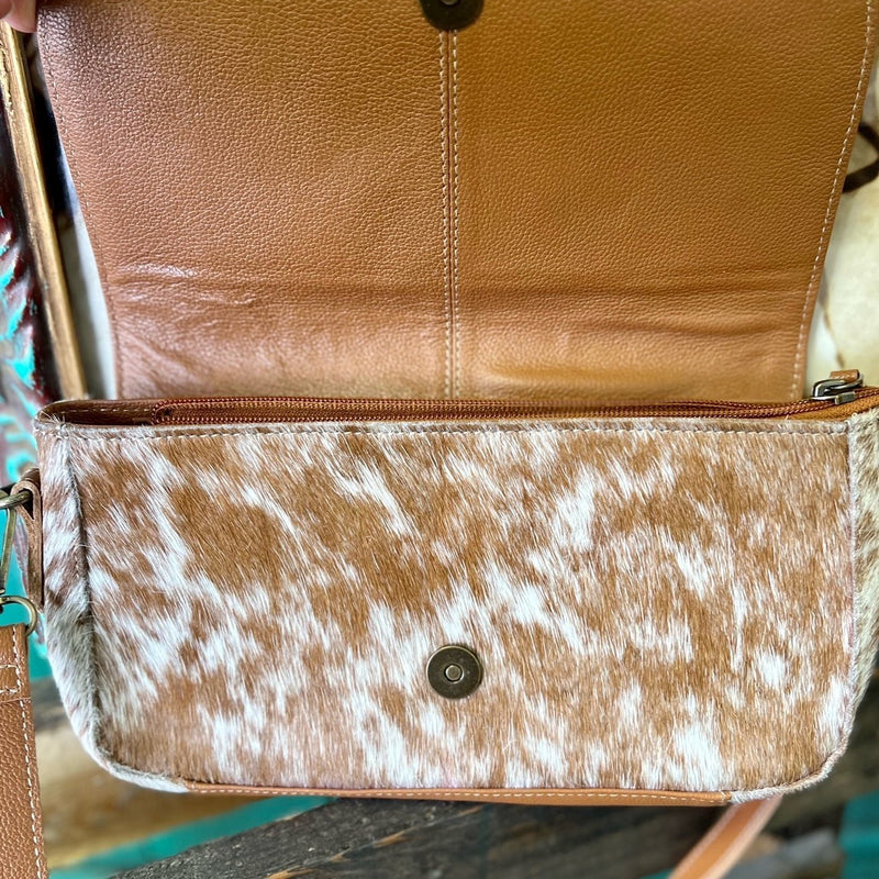 Made by Myra Handbags  The Los Lunas Cross Body Bag is a Beautiful Cowhide Purse with a Hand Tooled fold over flap. The Bag offers 3 different cowhide variants. This bag has a top zipper closure with a fold over flap.  The strap is a 44" and is adjustable/removable.  Dimensions: L 11" X H 6"   Adjustable up to 44"