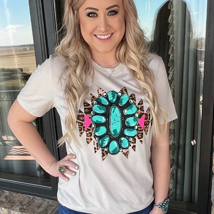 Wear your wild side on your sleeve with this tan tee featuring an eye-catching leopard Aztec design, a pink accent, and a giant turquoise concho! Get comfy and express your unique style with this one-of-a-kind shirt – it's sure to stand out from the crowd! This shirt does run a little smaller then most of our t-shirts.  This tee runs a tick smaller.   Meredith is wearing a Large  90% COTTON 10% POLYESTER