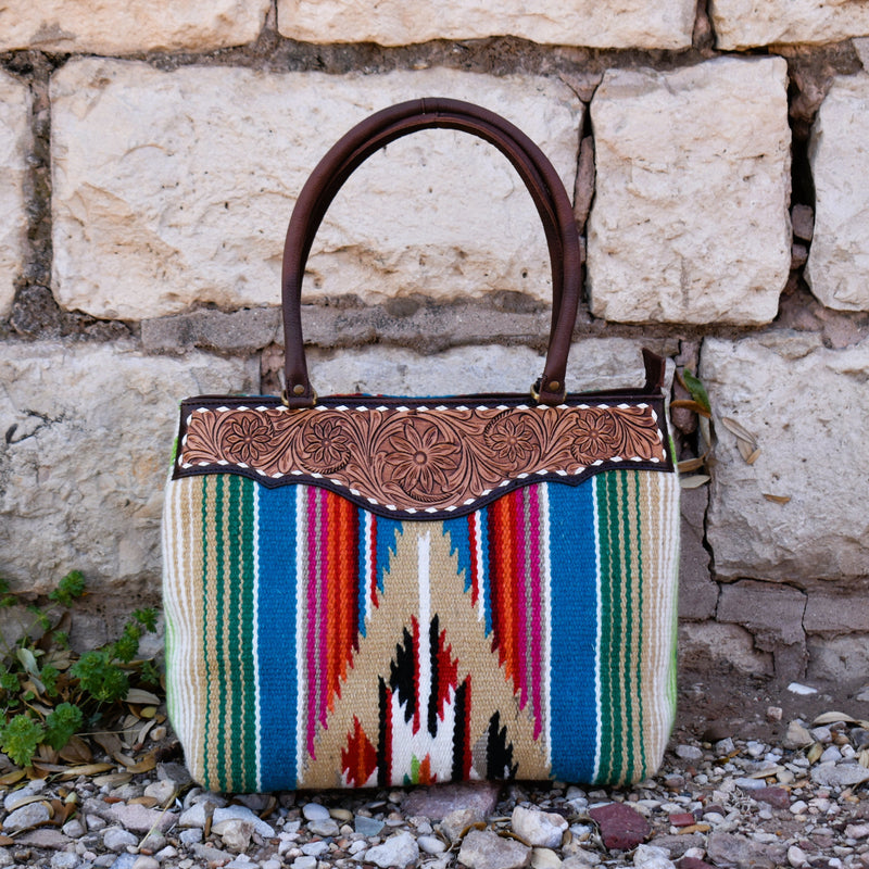 Multicolored serape saddle blanket bag with white buckstitch tooled leather top detail in the front. Padded double handles that are perfect to rest on your shoulder. Brass feet for durability and cleanliness. Zipper top closure.