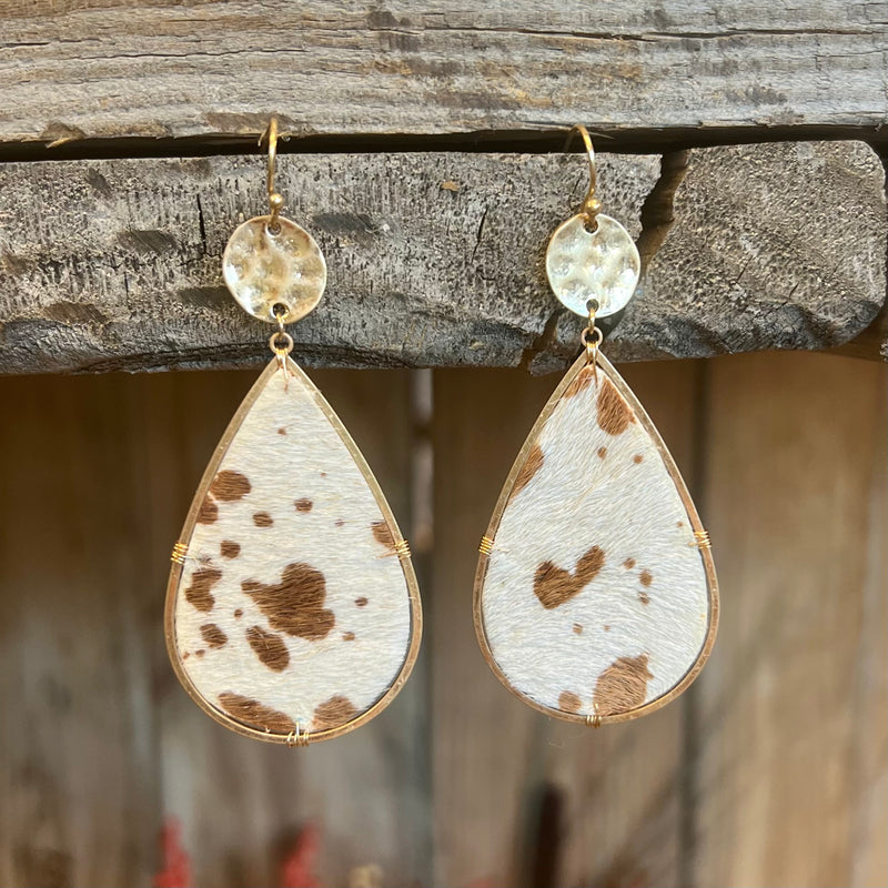 These Spotted Perfection Earrings come in 2 different colors. They are a black and white cow print cowhide and a brown and white cow print cowhide. They are a tear drop design attached to a small gold hammered circle on a fish hook.