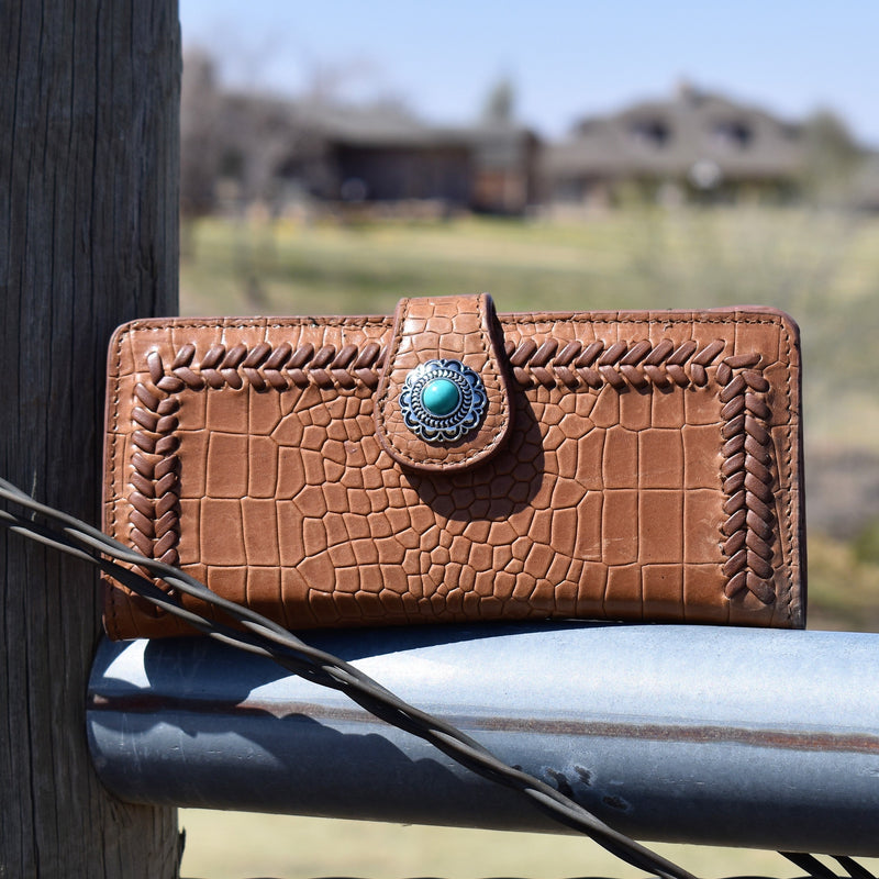 Large tan croc print embossed leather wallet with braided lacing detail. Silver concho and turquoise stone detail on the fold over strap and a snap button closure.   7.75"Wx3.5"H