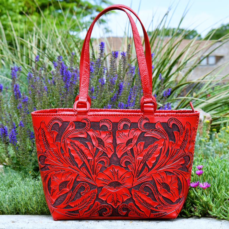 A timeless piece to add to your collection! This gorgeous and unique statement bag is all tooled leather and all yours! Red floral tooled front and basket weave tooled back are accentuated with a black patina. Embossed handles attached with leather covered D-rings for durability, and lacing along the seams. Top zipper closure. Suede lined inside, with two open pouch pockets and a zipper pocket.