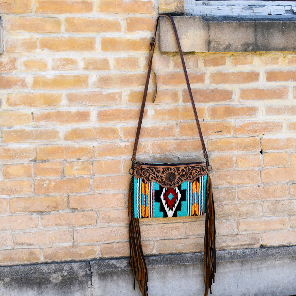 Beautiful and bright saddle blanket cross-body featuring brown leather fringe on the sides. Tooled leather front at the top showcasing a stunning sunflower motif. Bag is zipper closure, with small inside zipper pocket, small open pocket. Cross-body is strap is adjustable and removable.
